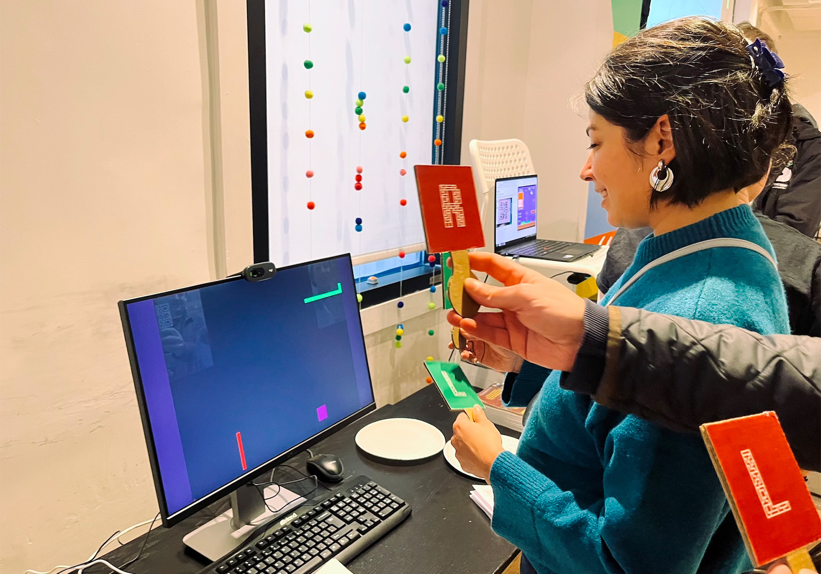 Two people holding QR codes on paddles up to a webcam in a game of Serpent Qrossing